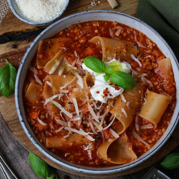 Eine Schüssel Lasagnesuppe mit breiten Nudeln, Ricotta und Basilikum garniert.