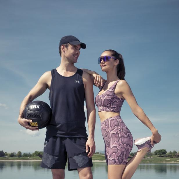 Ein sportliches Paar posiert mit einem Medizinball am See.
