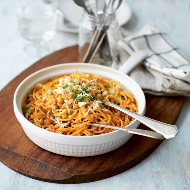 Eine Schüssel Spaghetti mit Erbsen, Tomatensoße und geriebenem Käse auf einem Holztisch.