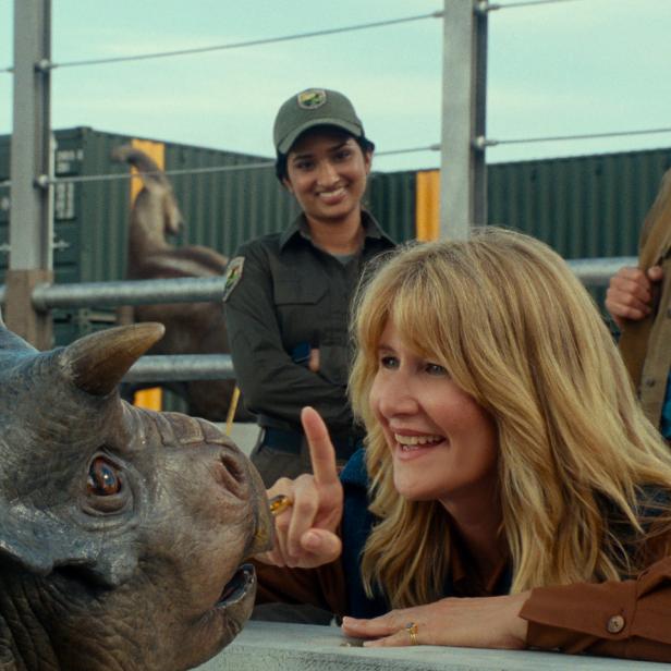Laura Dern interagiert mit einem Triceratops, während Sam Neill und eine Parkangestellte zusehen.