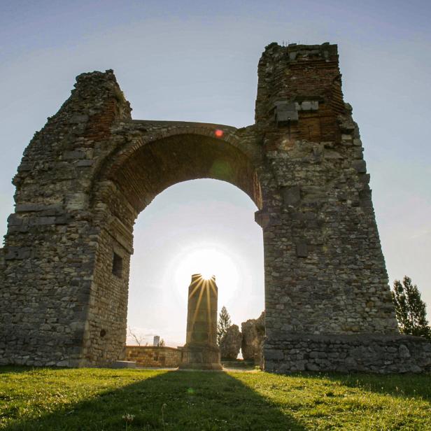 Die Ruine eines römischen Triumphbogens mit einem Obelisken im Gegenlicht.