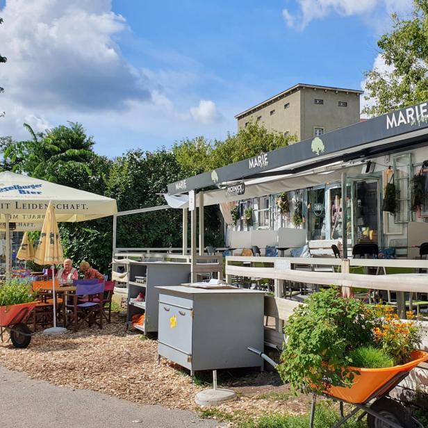 Einladender Außenbereich des Cafés „Marie“ mit bunten Stühlen und Sonnenschirmen.