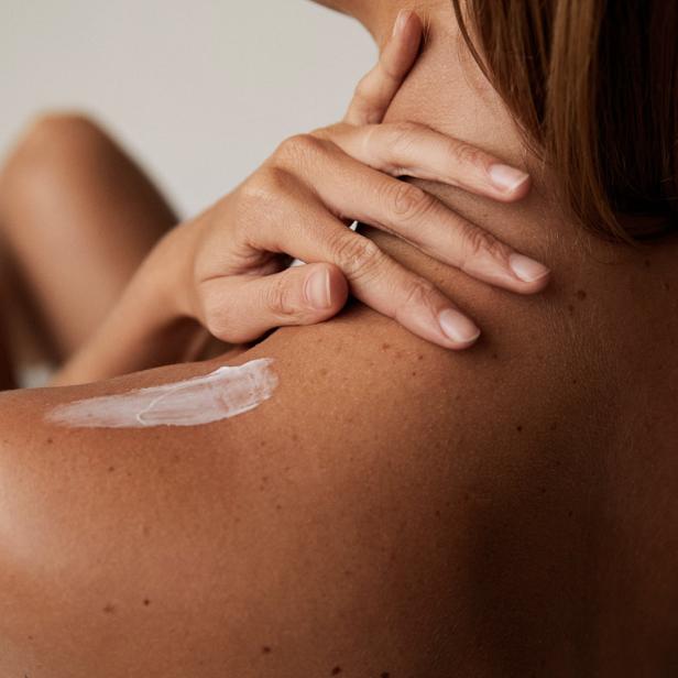 Eine Frau cremt ihre Schulter mit einer weißen Lotion ein.