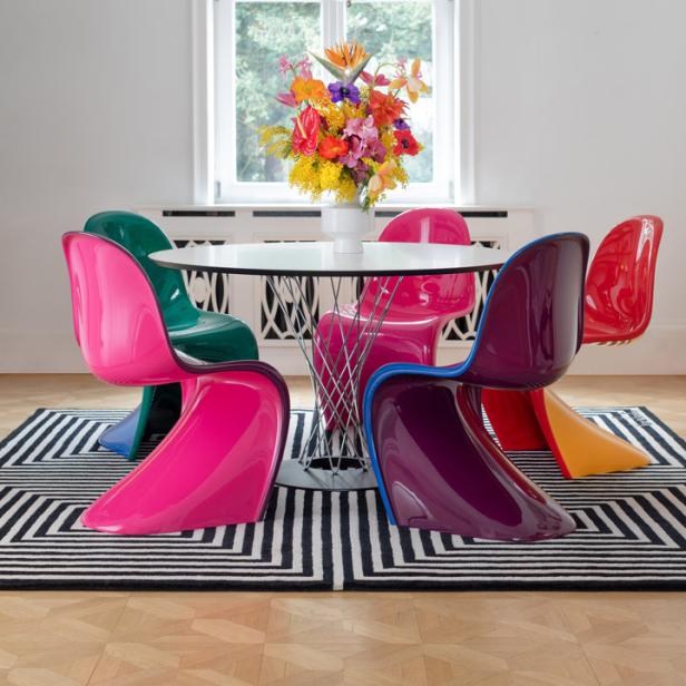 Ein Esstisch mit bunten Stühlen und einem Blumenstrauß unter einer modernen Lampe.