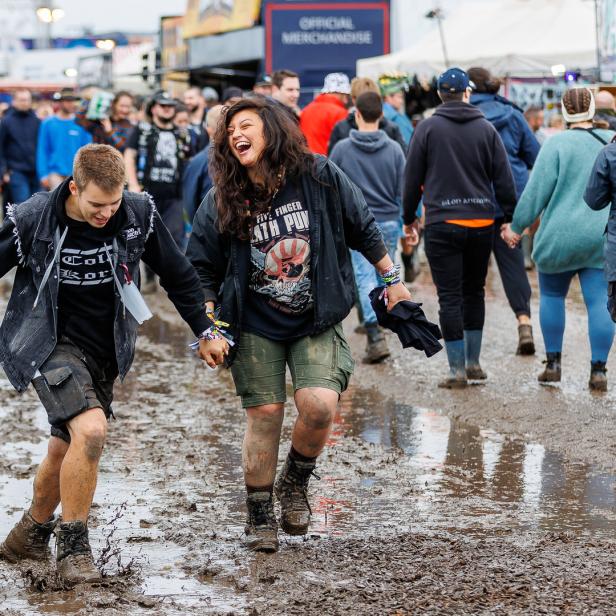 Zwei lachende Personen gehen Hand in Hand durch den Schlamm auf einem Festival.