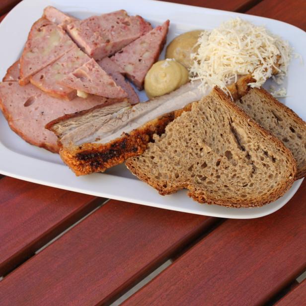 Eine Brotzeitplatte mit Leberkäse, Schweinebraten, Brot, Senf und Meerrettich auf einem Holztisch.