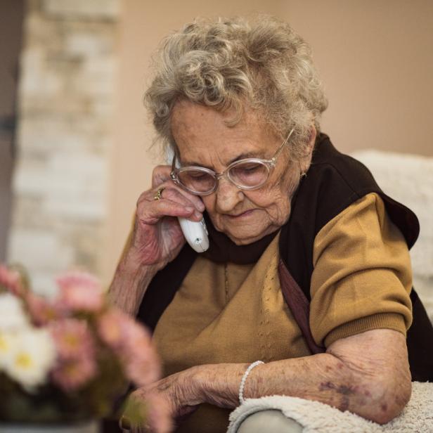 Eine ältere Frau mit Brille telefoniert mit einem weißen Telefon.
