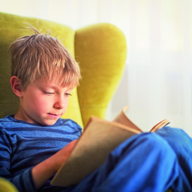 Ein kleiner Junge liest ein Buch in einem grünen Sessel.