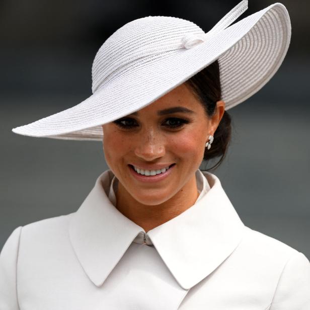 Meghan Markle mit einem weißen Hut und passendem Mantel lächelt.