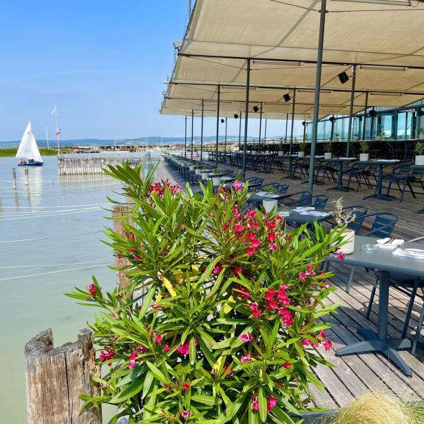 Ein Restaurant am See mit einem Segelboot im Hintergrund.