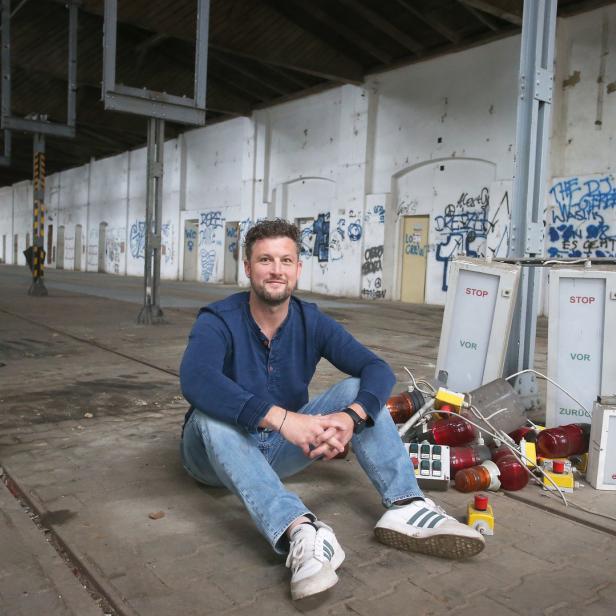 Ein Mann sitzt in einer alten Lagerhalle neben einer Sammlung von Signalleuchten.