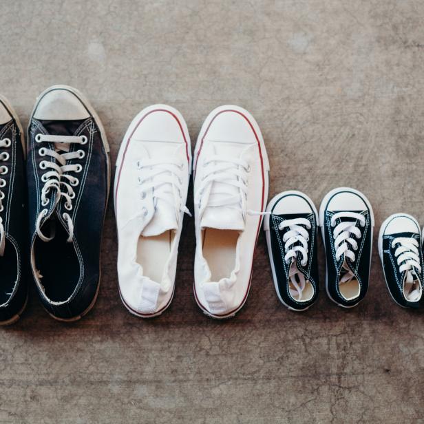 Drei Paar Converse-Turnschuhe in verschiedenen Größen stehen auf einem Betonboden.