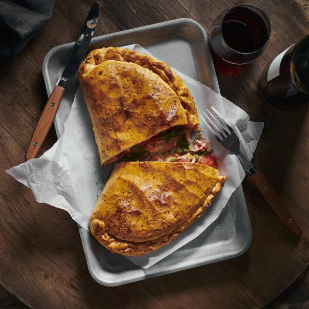Ein aufgeschnittener Calzone auf einem Serviertablett mit einem Glas Rotwein.