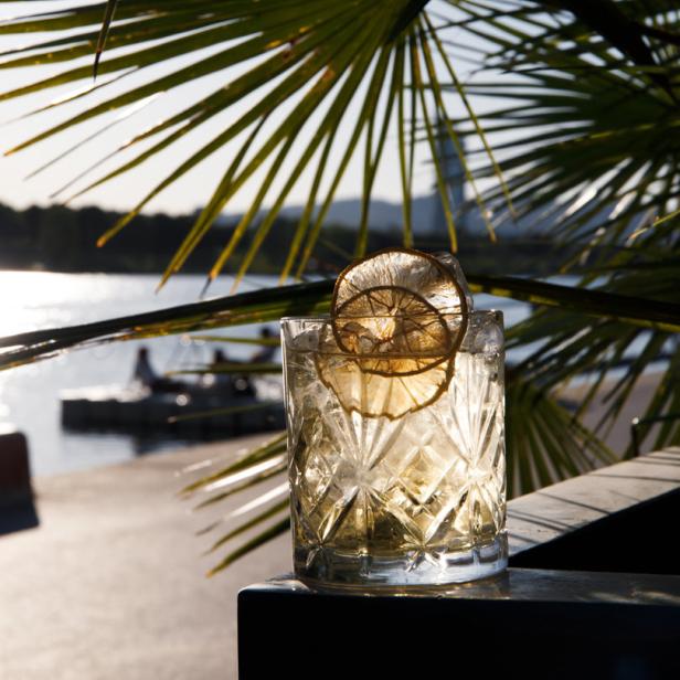 Ein Cocktail mit Eis und Zitronenscheiben vor einer Küstenlandschaft.