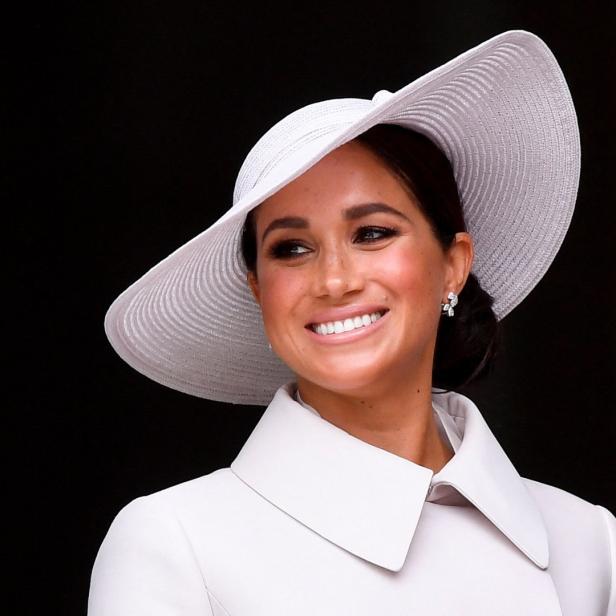 Meghan, Herzogin von Sussex, lächelt und trägt einen weißen Hut.
