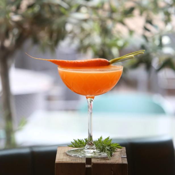 Ein orangefarbener Cocktail wird mit einer Karotte garniert serviert.