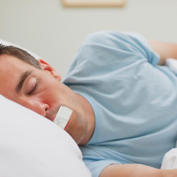 Ein Mann schläft mit einem Pflaster über dem Mund im Bett.