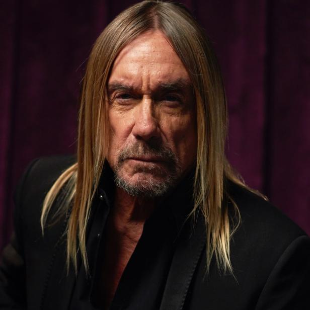 Porträt von Iggy Pop mit langem, blonden Haar und schwarzem Anzug vor einem violetten Hintergrund.