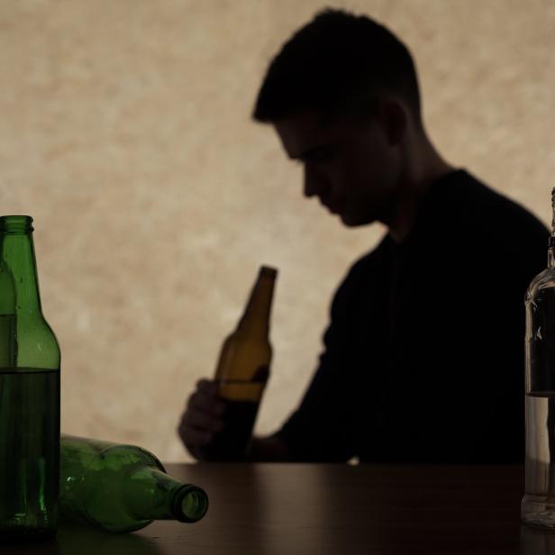 Ein junger Mann schaut auf eine Bierflasche.