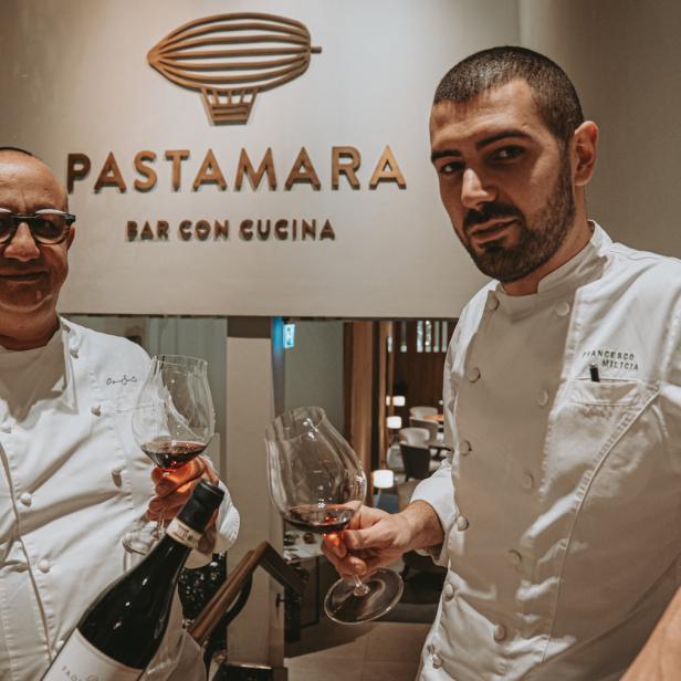 Zwei Köche im „Pastamara Bar con Cucina“ halten Weingläser in der Hand.