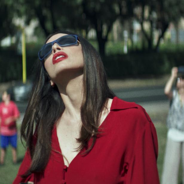 Eine Frau mit Sonnenbrille und roter Bluse blickt in den Himmel.