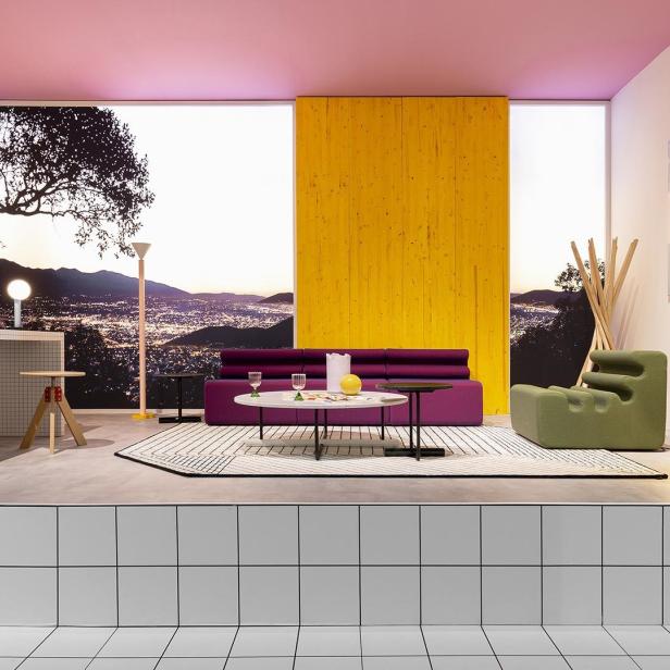 Ein farbenfrohes Wohnzimmer mit lila Sofa und Blick auf eine Stadt bei Dämmerung.