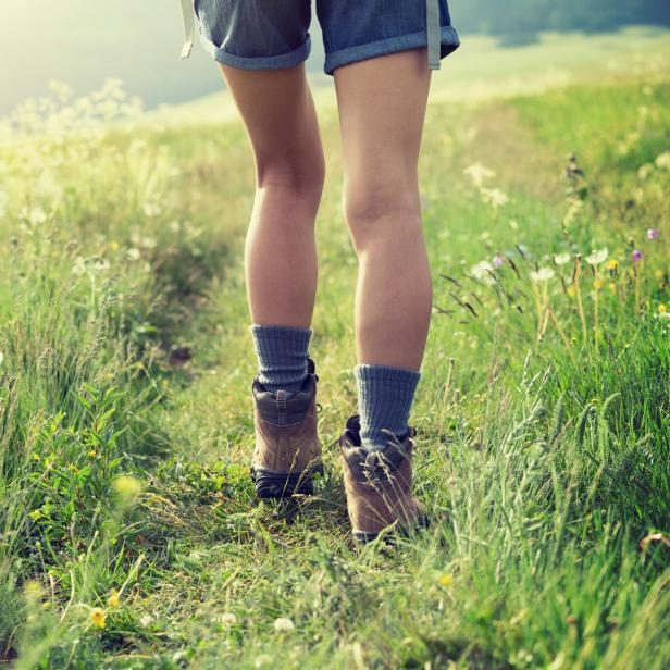 Eine Person wandert mit Wanderschuhen durch eine grüne Wiese voller Blumen.