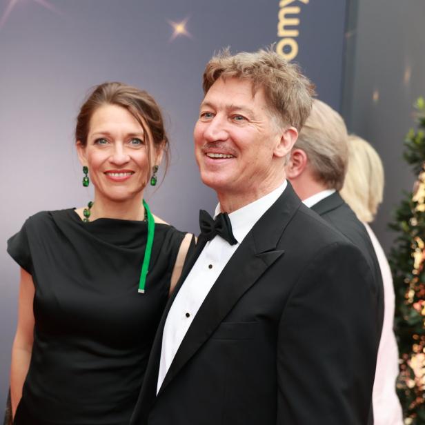 Ein Mann im Smoking und eine Frau im schwarzen Kleid posieren auf dem roten Teppich.