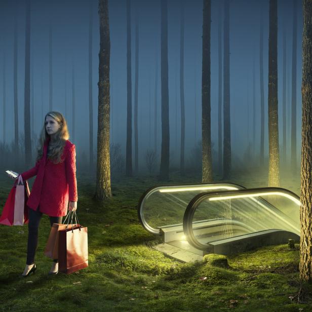 Eine Frau mit Einkaufstüten steht in einem Wald neben einer Rolltreppe.