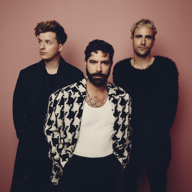 Die Band Foals posiert vor einem rosafarbenen Hintergrund.
