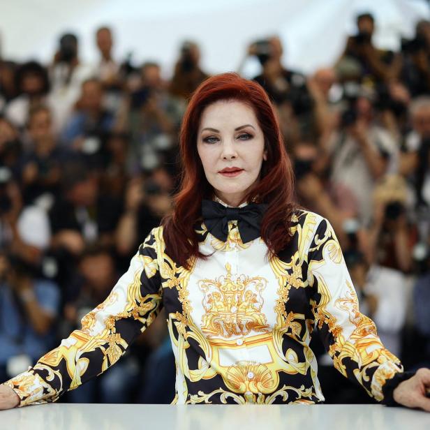 Priscilla Presley posiert vor einer Menschenmenge mit Kameras.