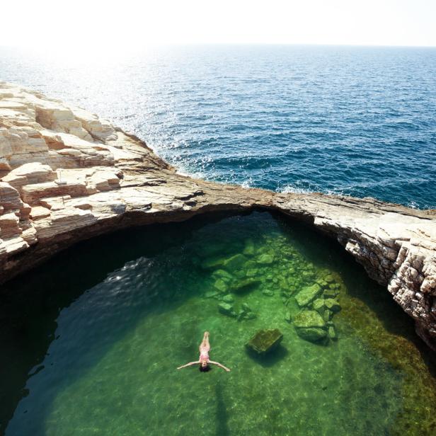 Eine Frau schwimmt in einem natürlichen Felsenpool am Meer.