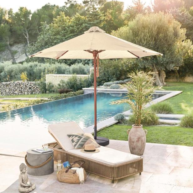 Ein Liegestuhl mit Sonnenschirm steht neben einem Pool in einem Garten.
