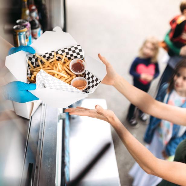 Eine Frau kauft an einem Imbisswagen eine Portion Pommes mit Dips für ihre Kinder.