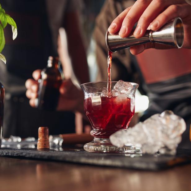 Ein Barkeeper mixt einen roten Cocktail mit Eiswürfeln in einem Glas.
