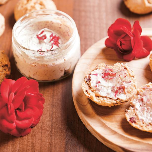 Ein Holzteller mit Brötchen, Aufstrich in einem Glas und roten Rosen.