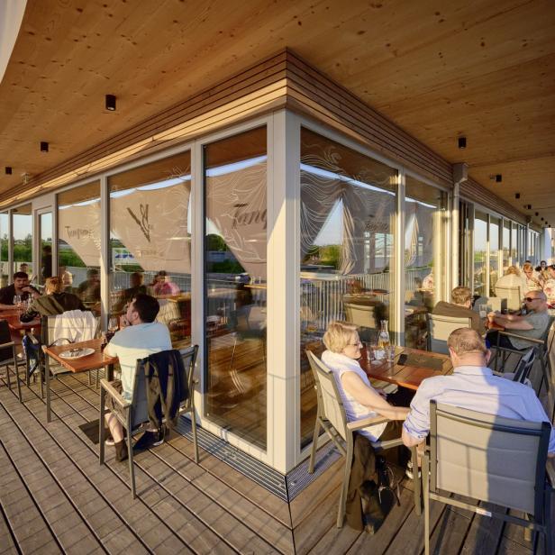 Gäste sitzen auf der Terrasse eines Restaurants mit Glasfront.