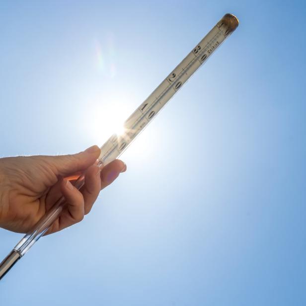 Eine Hand hält ein Thermometer vor blauem Himmel in die Sonne.