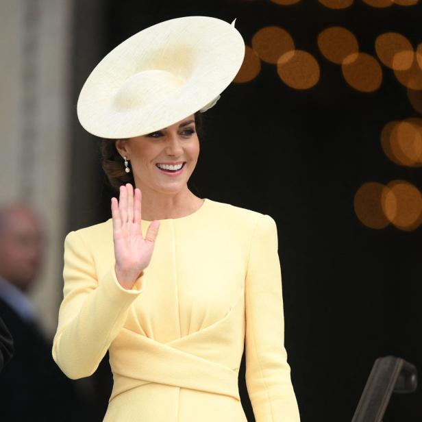 Kate Middleton trägt ein gelbes Kleid und einen Hut und winkt.