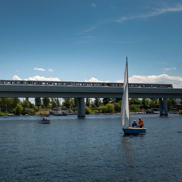 Eine U-Bahn fährt über eine Brücke, während ein Segelboot auf dem Wasser fährt.