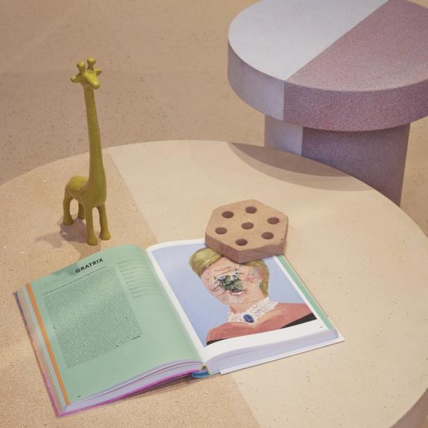 Ein Buch mit einem Porträt liegt auf einem runden Tisch, daneben eine Giraffenfigur.
