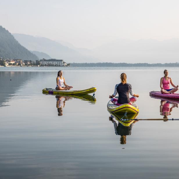 Vier Frauen machen Yoga auf Stand-Up-Paddle-Boards auf einem ruhigen See.