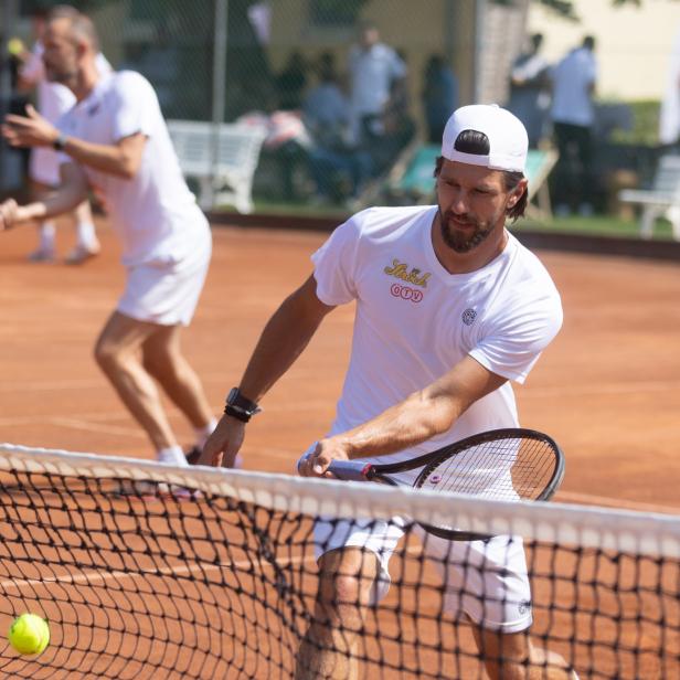 Ein Tennisspieler schlägt den Ball über das Netz auf einem Sandplatz.