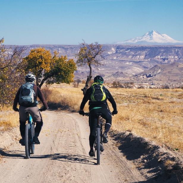 Zwei Radfahrer fahren auf einer unbefestigten Straße mit Blick auf einen Berg.