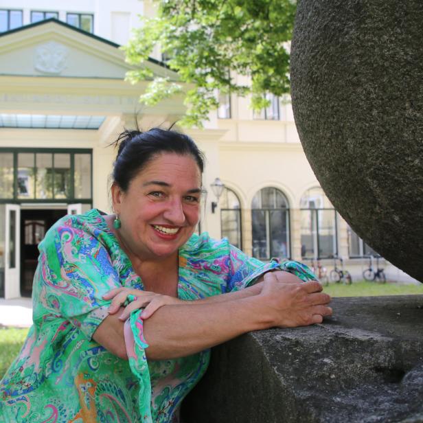 Eine lächelnde Frau lehnt an einer Steinkugel vor dem Max Reinhardt Seminar.