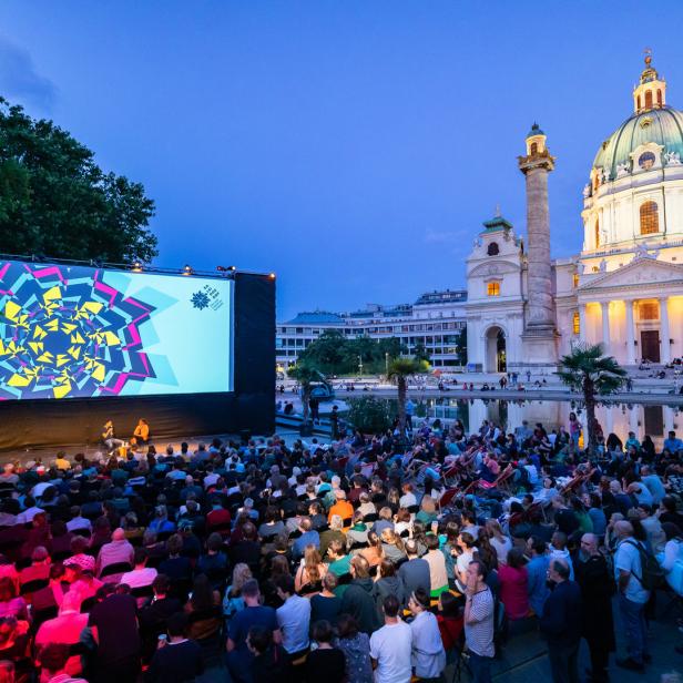 Eine große Menschenmenge schaut bei Dunkelheit einem Film vor der Karlskirche in Wien zu.