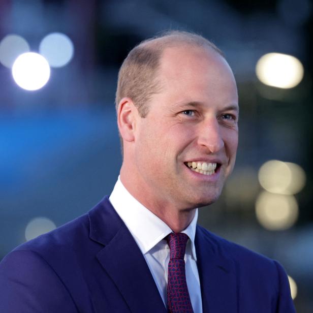 Prinz William lächelt in einem blauen Anzug und einer gemusterten Krawatte.