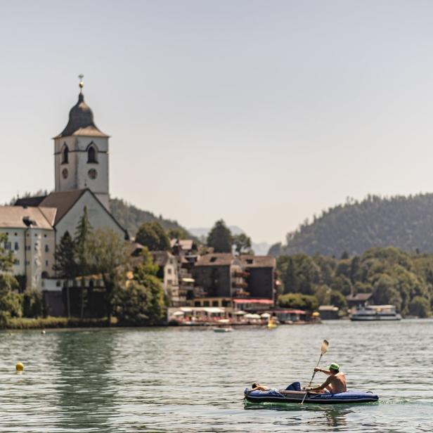 Ein Mann paddelt in einem Schlauchboot auf dem Wolfgangsee, im Hintergrund St. Wolfgang.