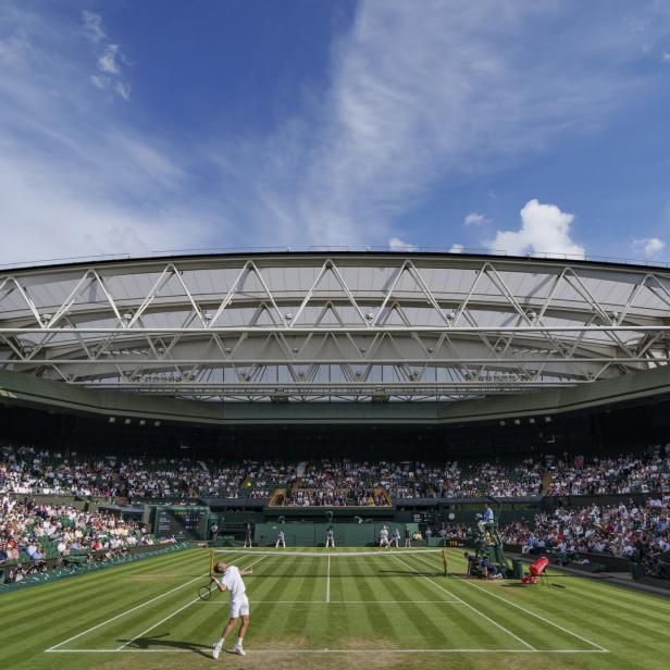 Ein Tennisspieler beim Aufschlag während eines Spiels in Wimbledon vor vollen Zuschauerrängen.