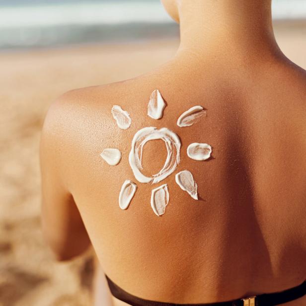 Sonnencreme in Form einer Sonne auf dem Rücken einer Frau am Strand.